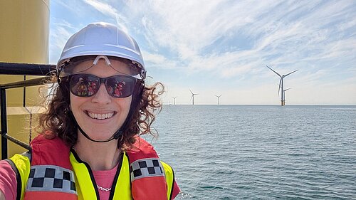 Alison in Hard Hat at Rampion wind farm with the sea stretching out into the background and several turbines