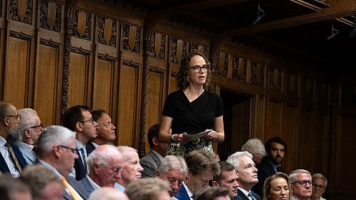 Alison Bennett MP asking a question in the parliamentary chamber, surrounded by sitting MPs