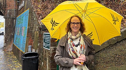 Alison holding a yellow umbrella outside Wivelsfield Station